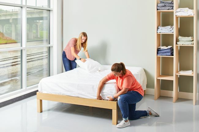 dwie kobiety ścielejące łóżko z białą pościelą